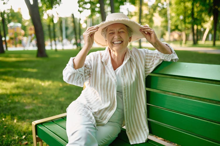 envejecimiento de la piel
Una adulta mayor disfruta del sol sentada en una banca en un parque mientras se toma con las manos un sombrero que lleva puesto