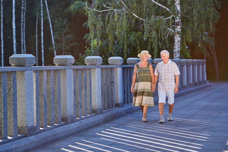 Dos adultos mayores pasean felices tomados de la mano en una zona con clima cálido.