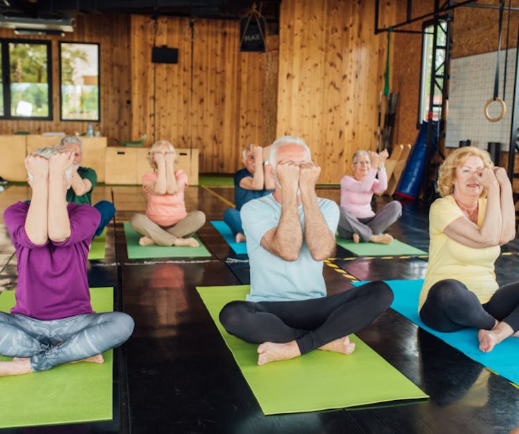 Muchas residencias de mayores tienen disponibles promociones de verano.
Un grupo de adultos mayores realizan ejercicios sentados sobre unos mantos en un salón.